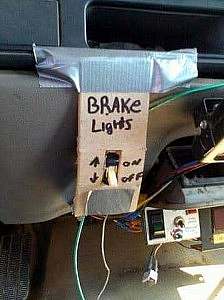 In a car is a piece of cardboard duct-taped to the dashboard. It is in the shape of a backplate with a switch in the middle. With a black marker is written at the top, "Brake lights; next to the top of the switch is "On" and next to the bottom of the switch is "Off"