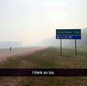 a very foggy road ahead among the mountains. Sign to the right says, "Little Smoke 1KM" Caption: I think so too.