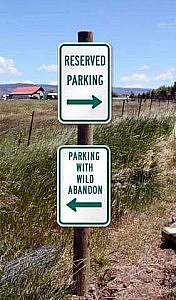 2 signs on a post. Top sign says RESERVED PARKING with an arrow pointing to the right. Bottom signs says PARKING WITH WILD ABANDON with an arrow facing to the left.
