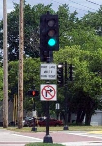 A stop light on a streetcorner; the light is green .Below the light is a sign: "Right land MUST turn right." Below that sign is another sign of a right-turn arrow, with a red circle around it and a line through it.