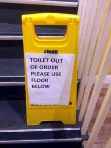 Yellow sign on some stairs, with a white paper attached to the front, saying, "Toilet out of order. Please use floor below."