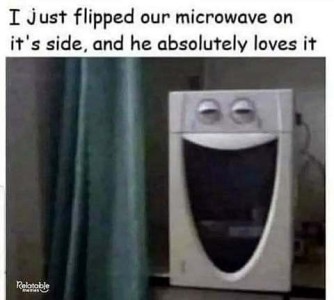 A machine sitting on a counter that looks like it has two slitted eyes and a wide-open happy smile. Caption: I just flipped our microwave on its side, and he absolutely loves it.
