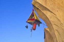 Someone in a small tent that is hanging beneath the overhang of a cliff. There is no door, or other protections from the height.