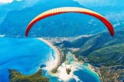 someone paragliding way up over mountains at the edge of an ocean