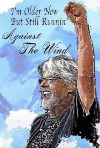 Chest up drawing of an older man with longer white hair and beard, glasses, and a black t-shirt; he has a confident smile on his face and his fist high in the air. Caption: I'm older now but still runnin' Against The Wind.