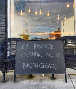 A chalkboard in front of a restaurant with the words, "My favorite essential oil is bacon grease."