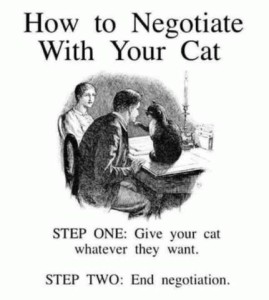 Title: How to Negotiate With Your Cat. A black and white drawing of a man and a woman sitting at a table. There is a cat sitting in front of the man, its paw on his chin. Caption: Step One - give your cat whatever they want. Step two - End Negotiation.