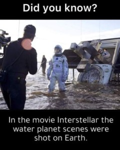 A movie set, in the water, showing a crashed piece of equipment, a man in an astronaut suit, a director, and someone holding a cable or something; there is a camera off to the side. Caption: Did you know? In the movie Interstellar the water planet scenes were shot on Earth.