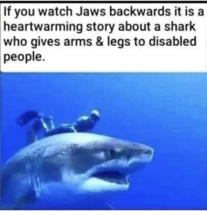A huge shark underwater with a man in a full scuba suit on his back; the shark looks fierce. Caption: If you watch Jaws backwards it is a heartwarming story about a shark who gives arms and legs to disabled people.