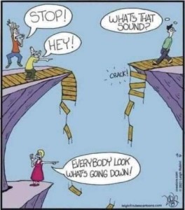 cartoon with 2 cliffs; the walking bridge between them is broken. On the left are two guys yelling across the to a guy on the right who isn't paying attention to where he is going. They are yelling, "STOP!" "HEY!" and the guy walking toward the broken bridge is looking behind him thinking, "What's that sound?" A woman on a cliff below is pointing to the broken bridge pieces falling past her, saying, "Everybody look what's going down!"
