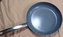 A frying pan with a gray interior and a long silver handle.