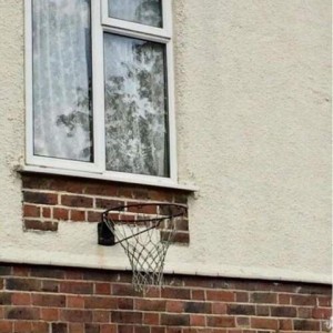 Photo of a window on the side of a building with a basketball hoop hanging directly under it.