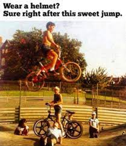 Old yellowed photo of kids playing, some on bikes, with ramps in the photo. One young boy is high up in the air on his bike. Caption: Wear a helmet? Sure right after this sweet jump