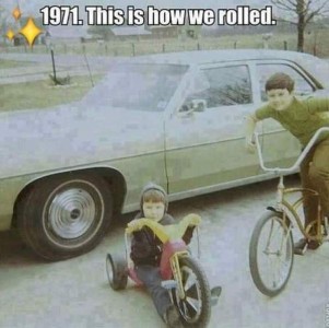 Vintage photo of a green car, with two boys in the foreground; one is on a bike, and one is on a Big Wheels.