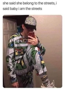 Caption: she said she belong to the streets, i said baby i am the streets. Photo of a young man taking a selfie, wearing pajamas and a baseball cap that are covered in street maps.
