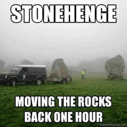 photo of a van with a huge rock on a trailer, a worker directing the truck as it backs up to another huge rock. Text: Stonehenge: moving the rocks back one hour.