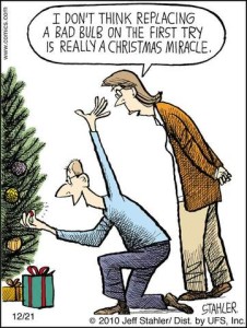 Cartoon of a man squatted down at a Christmas tree working on the lights; he looks very happy, with one arm up in the air. His wife stands behind him, looking down at him and saying, "I don't think replacing a bad bulb on the first try is really a Christmas miracle."