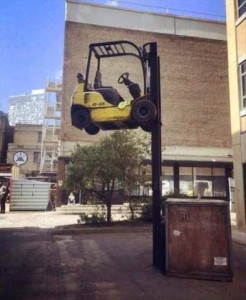Photo of a fork lift with an apparently very heavy wooden box on the prongs; the machine itself is about 10 feet up in the air.
