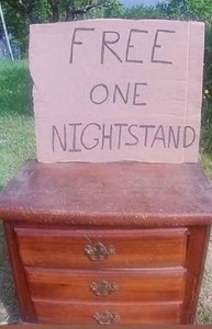 Photo of a small wooden cabinet with 3 drawers in the front; on top is a piece of cardboard with words hand printed on it: FREE. ONE NIGHTSTAND.