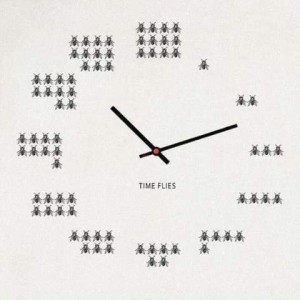 A clock that has little house flies in place of the numbers, one fly at 1:00, 2 flies for 2:00, etc., with the words TIME FLIES near the center.