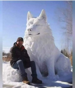 Photo of a man sitting on a pile of snow on a sunny day; next to him is a magnificent snow sculpture of a husky- or wolf- like dog, probably about 6 feet tall.