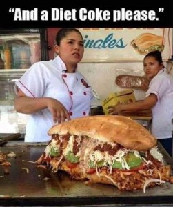 Photo of 2 women working in a restaurant; one of them is standing behind a massive sandwich loaded with meats, cheeses, avacado, etc.; the sandwich is about 3 feet long and a least a food wide and high. Caption: "And a diet Coke please."